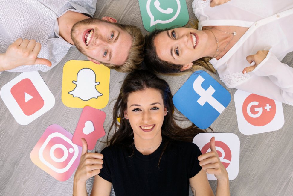 Grupo de 3 personas felices con diferentes símbolos de redes sociales que simboliza la promoción de un negocio en redes sociales