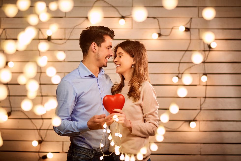 Una pareja sosteniendo un corazón rojo entre ellos creando un ambiente romántico perfecto para un anuncio de san valentín